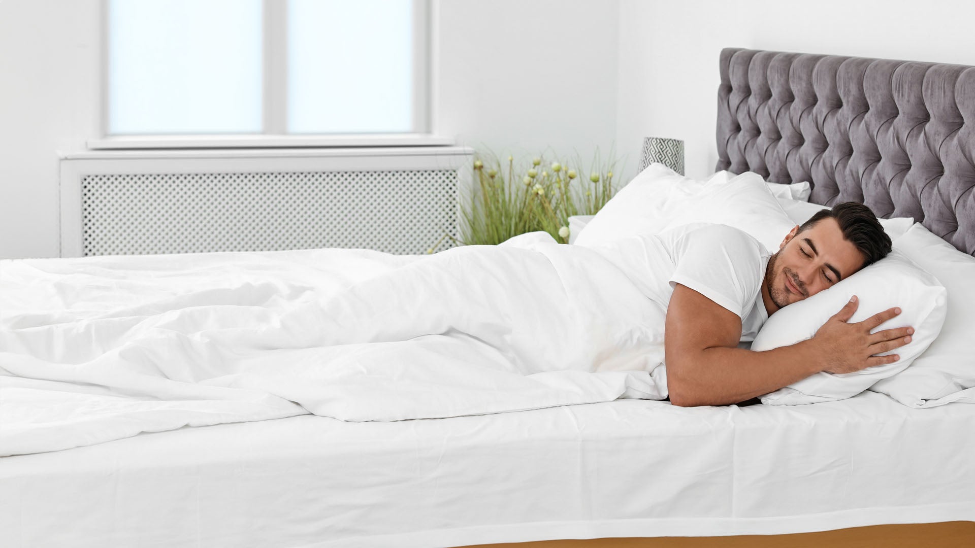 Dieses Bild veranschaulicht einen glücklichen Mann im Bett mit Bettdecke und Bettkissen.