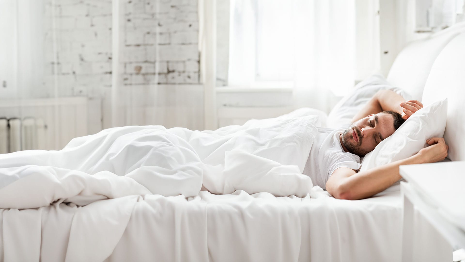 Dieses Bild veranschaulicht einen jungen Mann im Bett auf einem Rückenschläferkissen.